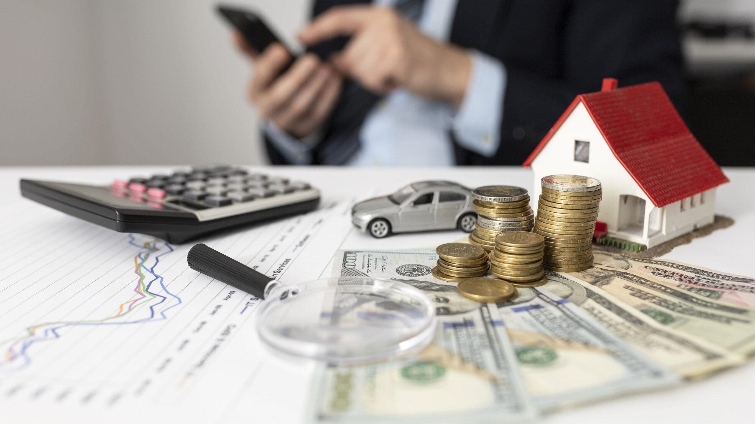 table with miniature house and car, money and a calculator.