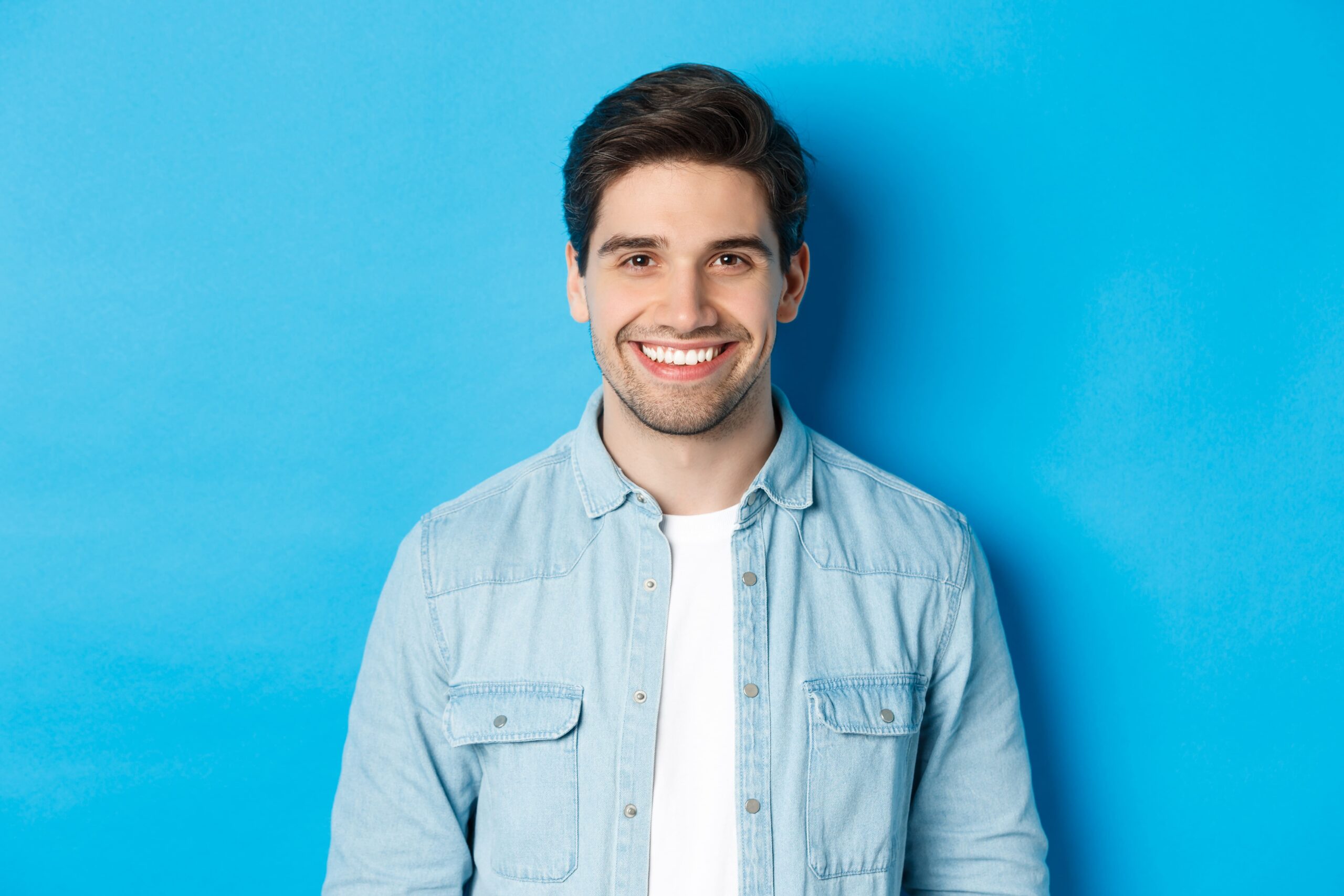 close-up-young-successful-man-smiling-camera-standing-casual-outfit-against-blue-background