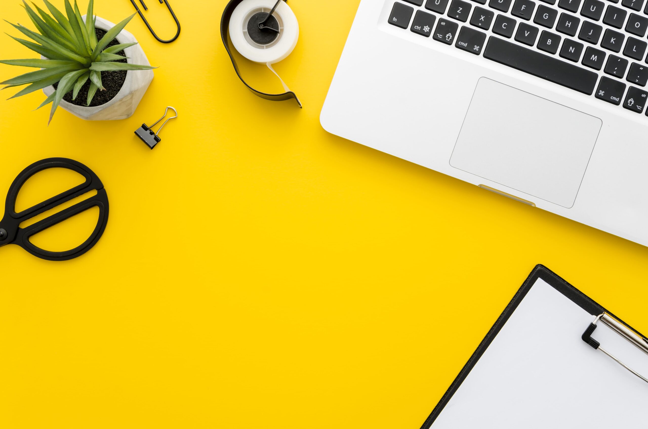 yellow desk with laptop, notepad and office supplies.